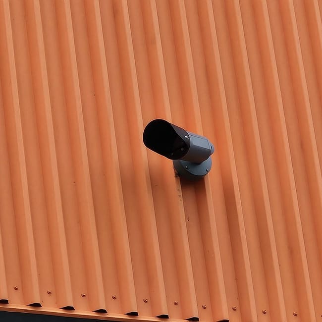 Security camera mounted on orange corrugated metal wall of building exterior