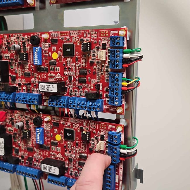 Red circuit boards with blue terminal blocks mounted in control panel for building automation system