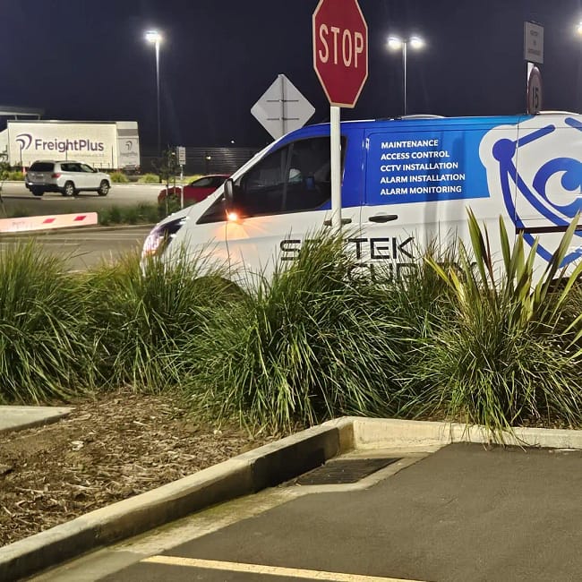 White and blue security van with maintenance services text parked at night intersection with stop sign
