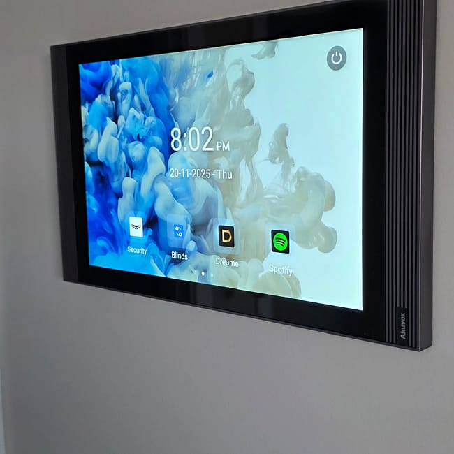 Wall-mounted smart home control panel displaying time, date, and app icons including Security, Blinds, Dreame, and Spotify