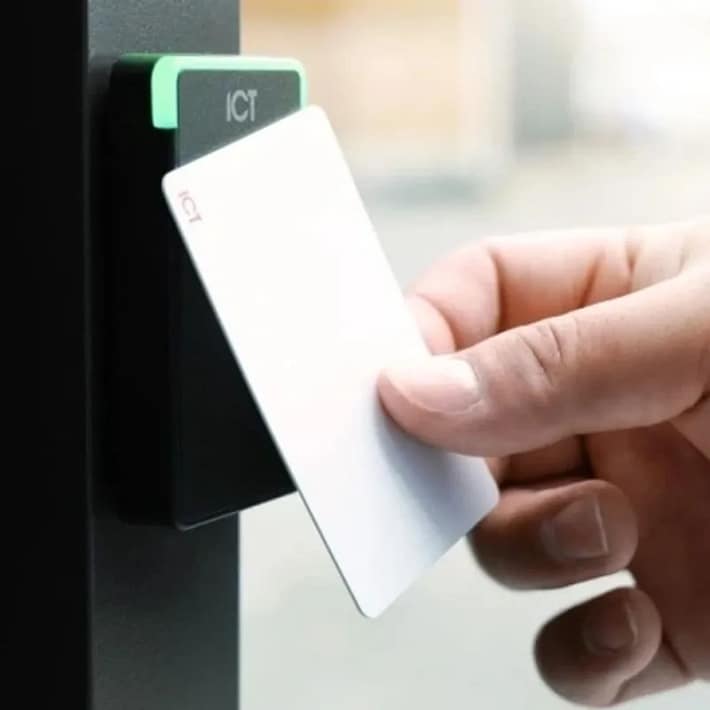 Person holding white access card near electronic card reader for secure door entry system